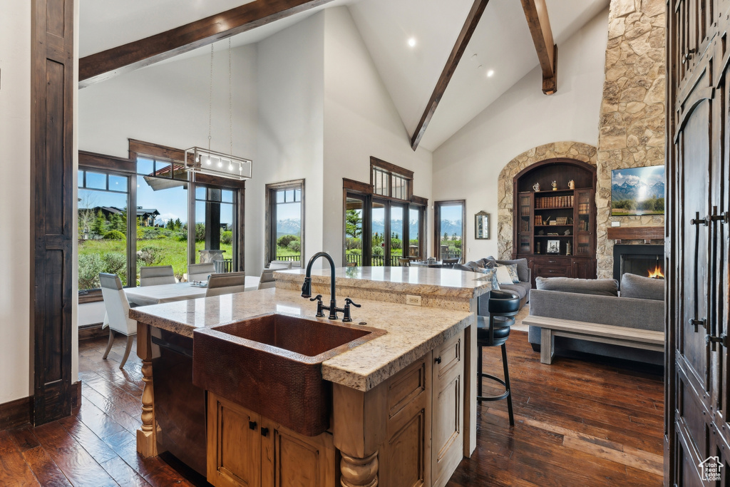 Kitchen with a sink, open floor plan, high vaulted ceiling, beam ceiling, and a large fireplace