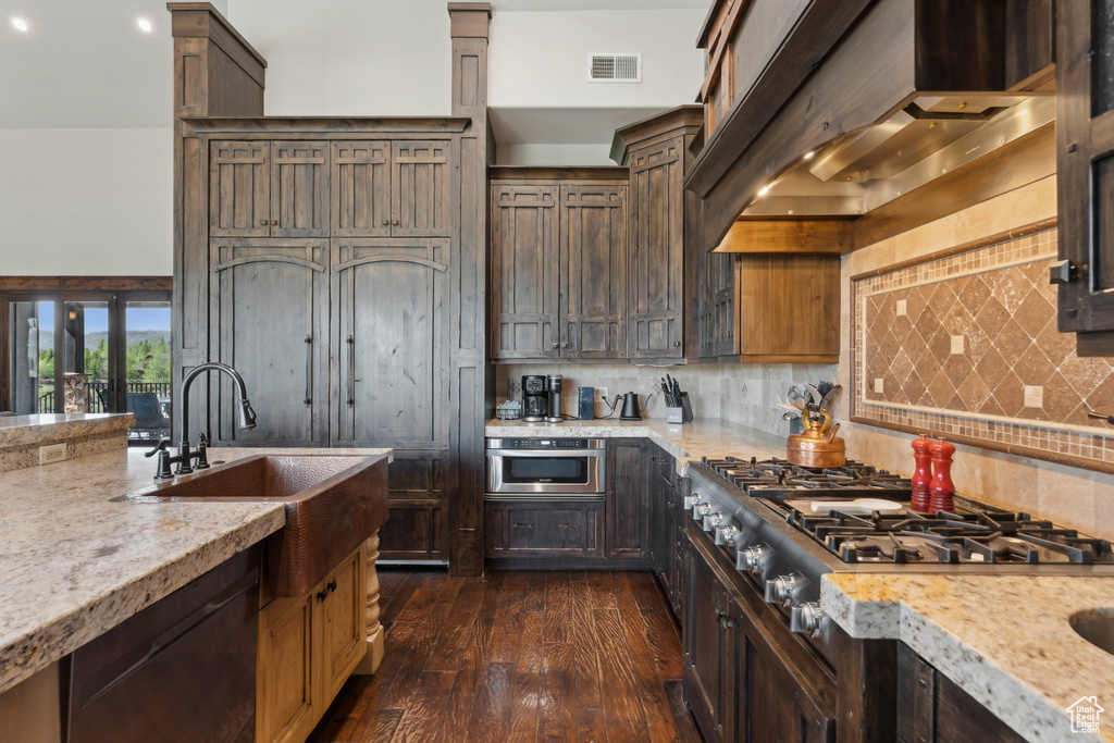 Kitchen featuring stainless steel gas stovetop, dishwashing machine, dark wood-type flooring, wall chimney range hood, and backsplash