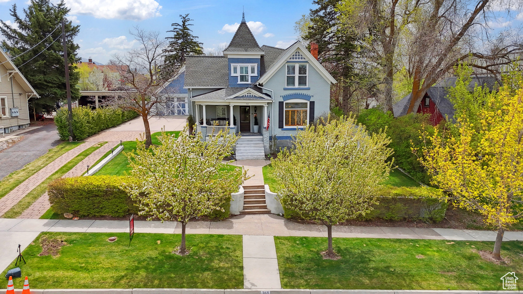 Victorian-style house with a porch, roof with shingles, stairs, and a front yard