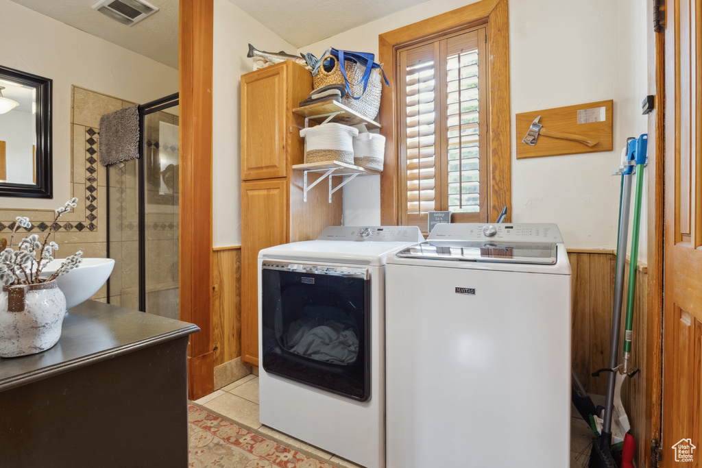 Clothes washing area featuring wainscoting, washer and dryer, cabinet space, wood walls, and visible vents