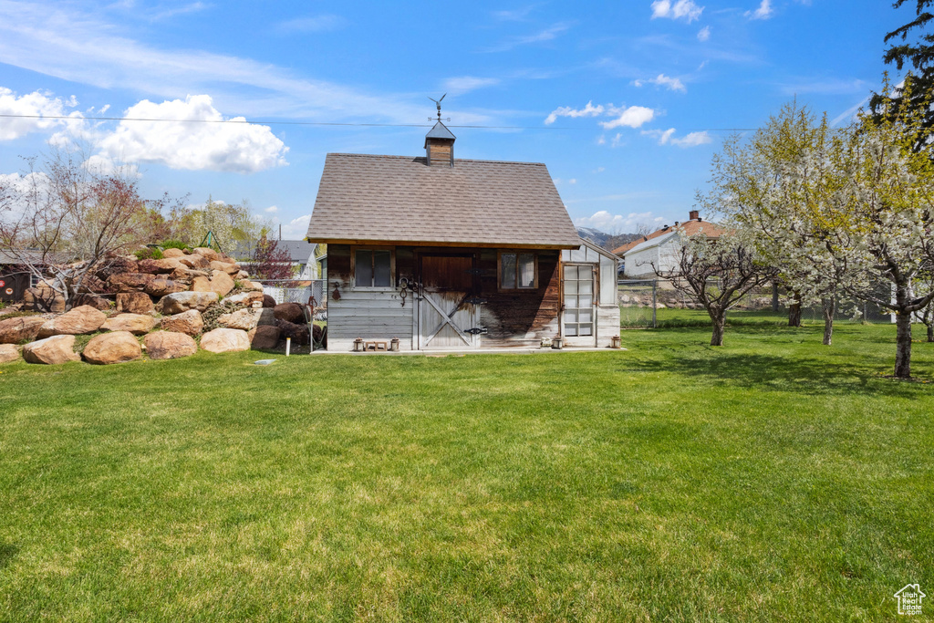 Back of house with roof with shingles, an outbuilding, and a lawn