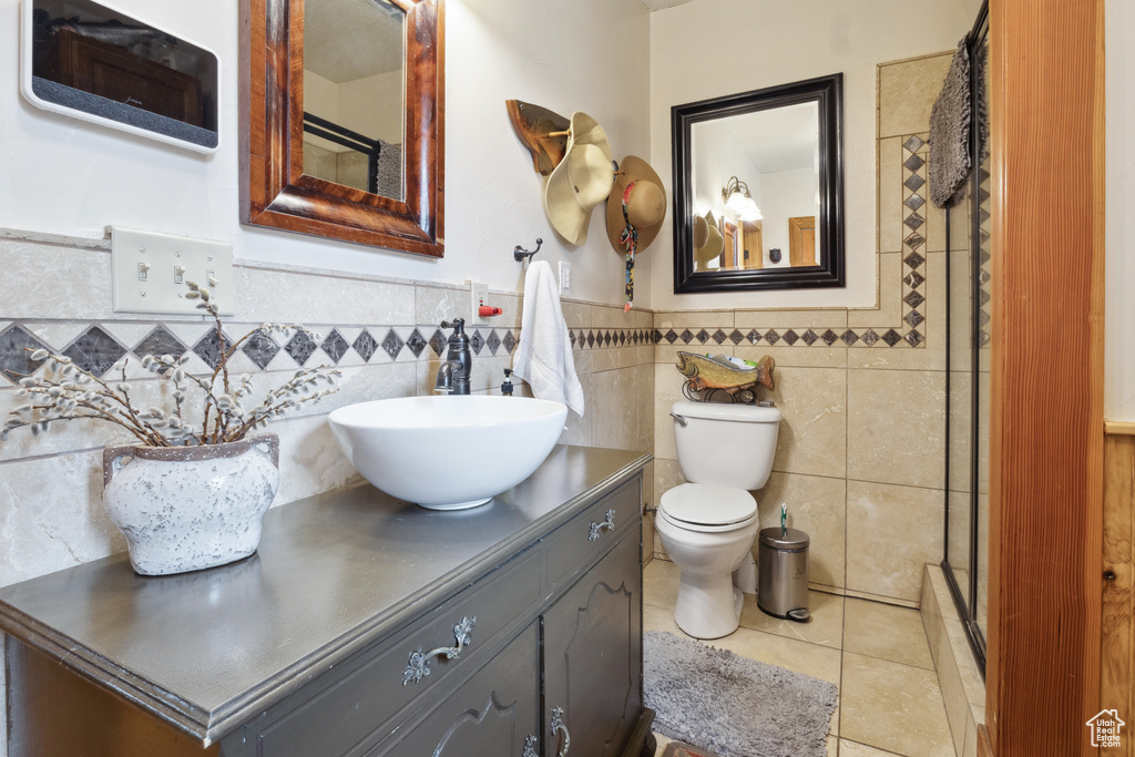 Bathroom with a wainscoted wall, a shower with door, tile walls, tile patterned floors, and vanity