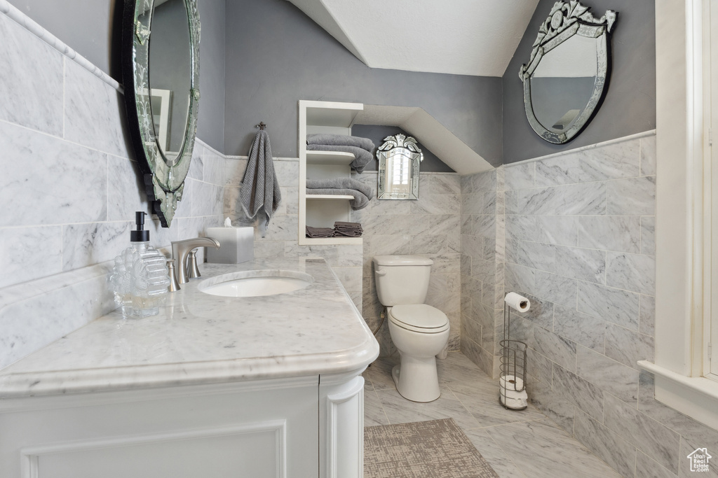 Bathroom with toilet, tile walls, a sink, and wainscoting