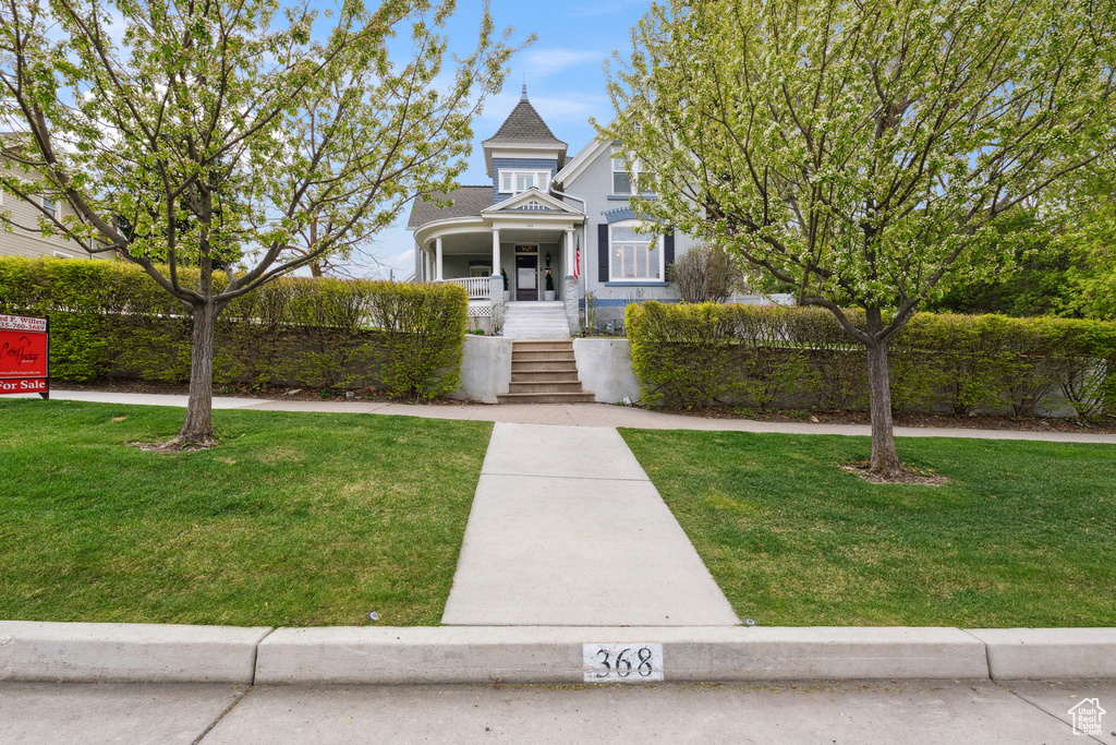 Victorian house with covered porch, a front yard, and stairs