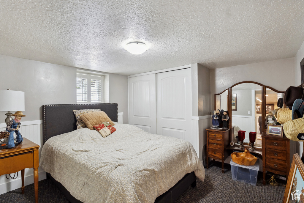 Bedroom featuring a closet, wainscoting, dark colored carpet, and a textured ceiling
