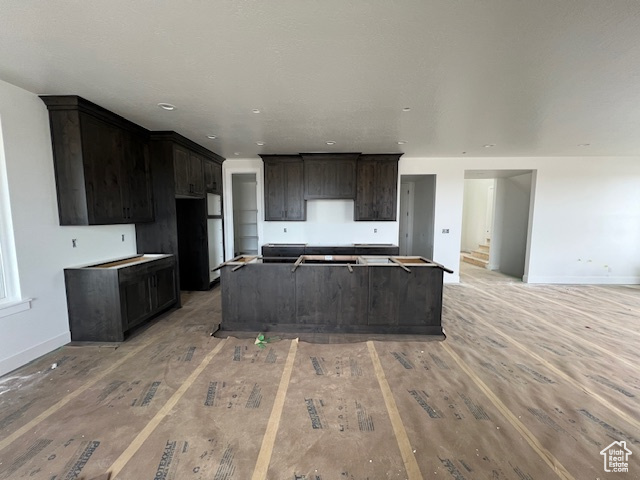 Kitchen featuring a kitchen island, light wood finished floors, baseboards, and dark brown cabinetry