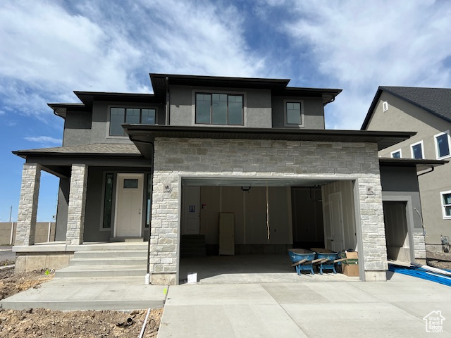 Prairie-style home with stone siding, concrete driveway, and stucco siding