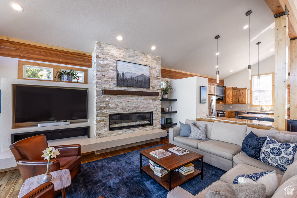 Living area with wood finished floors, lofted ceiling, a healthy amount of sunlight, and a stone fireplace