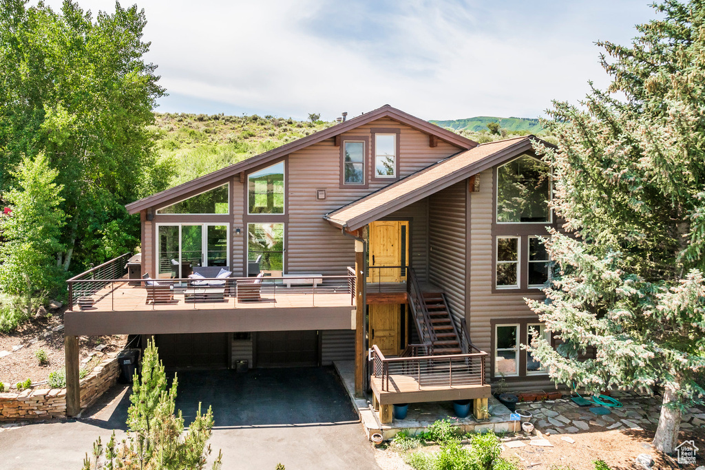Rear view of property featuring a deck, asphalt driveway, and stairs