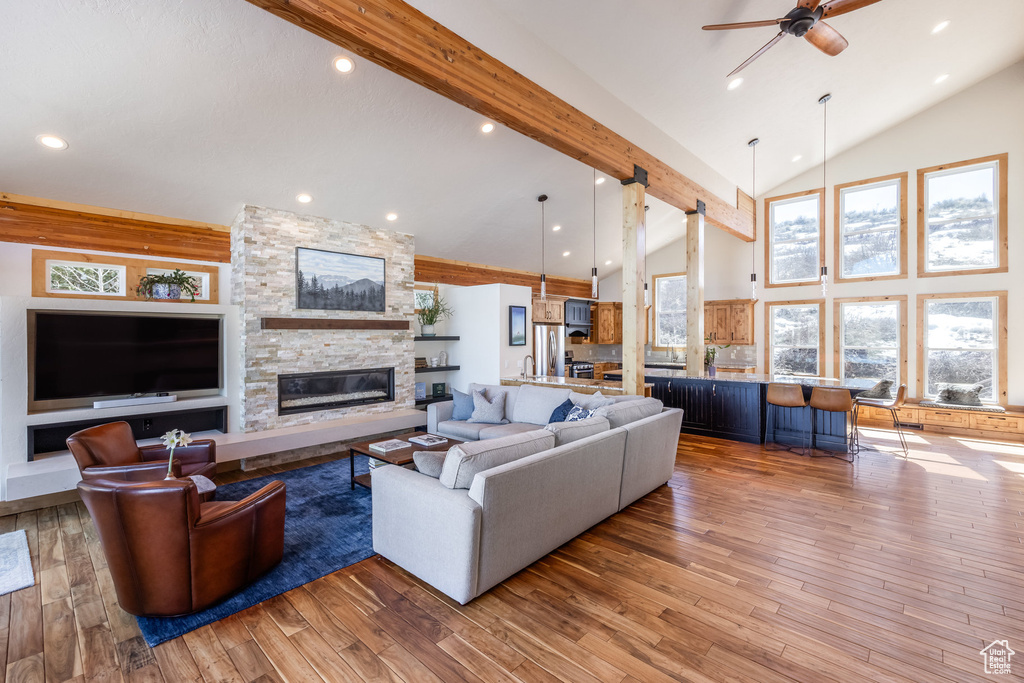 Living area with high vaulted ceiling, a ceiling fan, light wood-style floors, a stone fireplace, and beam ceiling