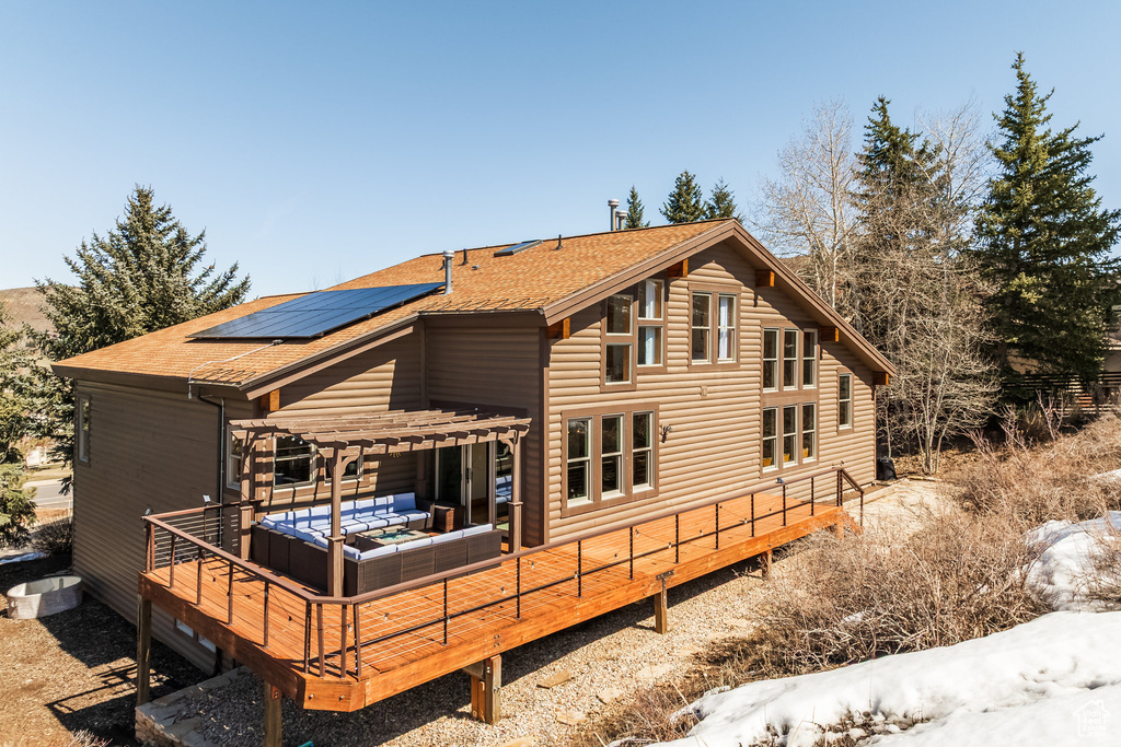 Back of property with an outdoor hangout area, a pergola, roof mounted solar panels, and roof with shingles