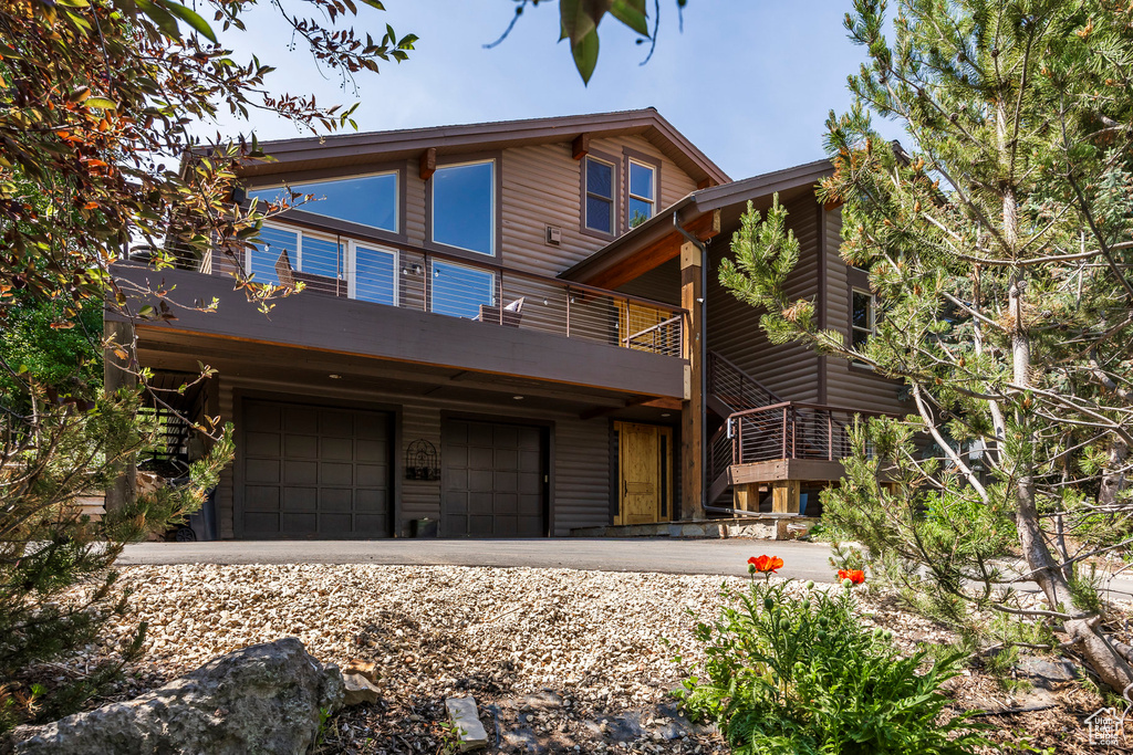 Rear view of property with a balcony, an attached garage, and driveway
