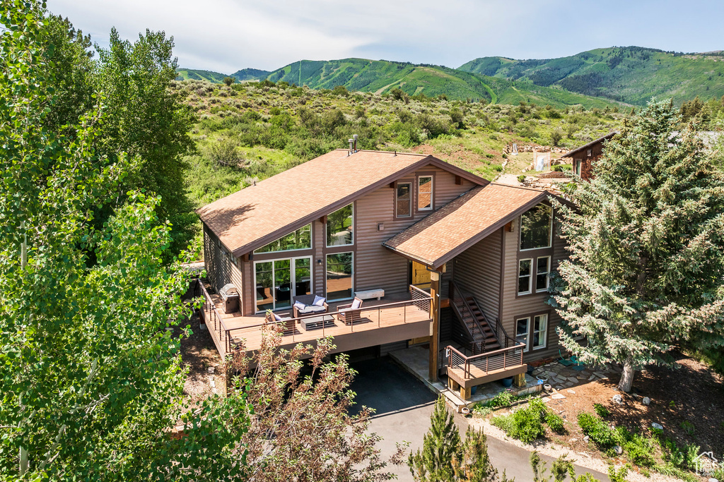 View of front facade with a deck with mountain view, a shingled roof, stairs, driveway, and a carport