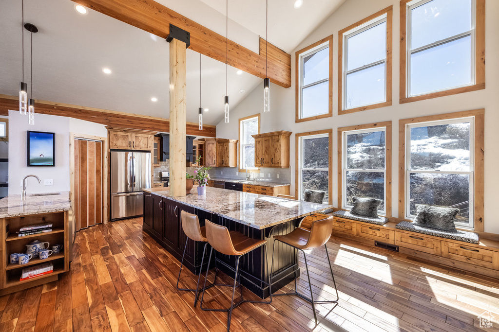 Kitchen with freestanding refrigerator, high vaulted ceiling, a spacious island, and light stone countertops