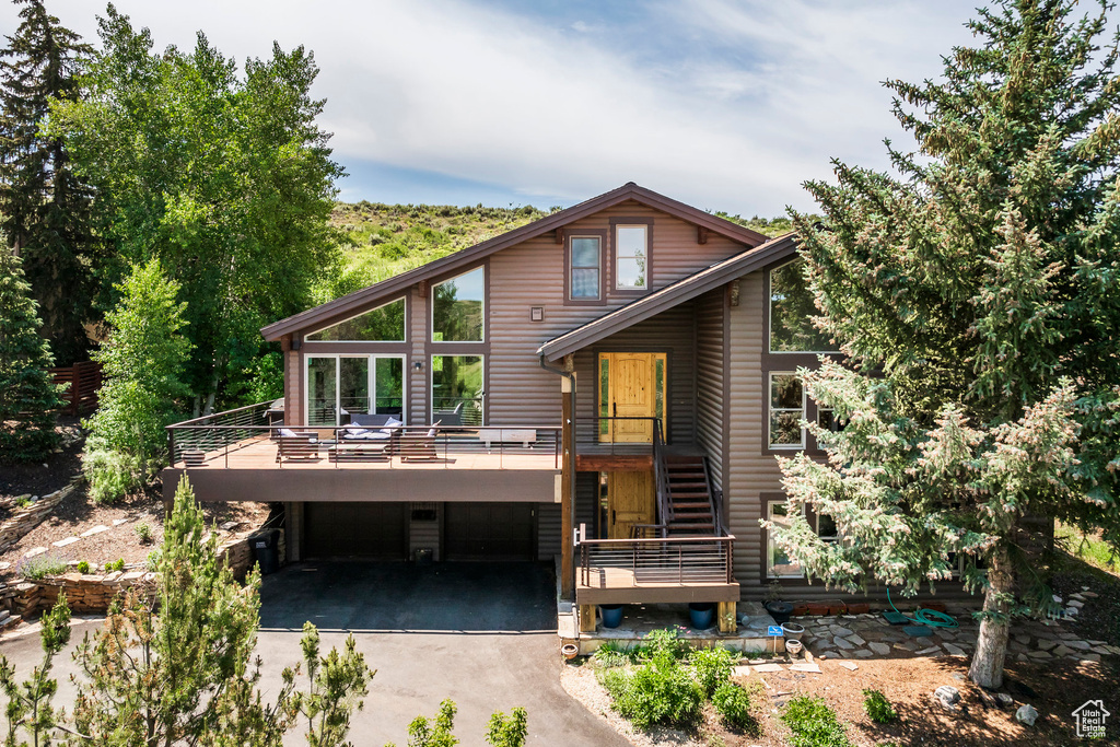 Rear view of house featuring a garage, asphalt driveway, stairs, and a wooden deck