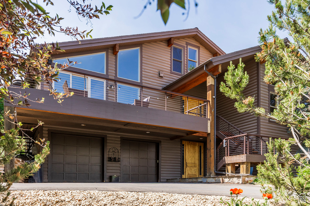 View of front of property with an attached garage, log veneer siding, a balcony, and driveway