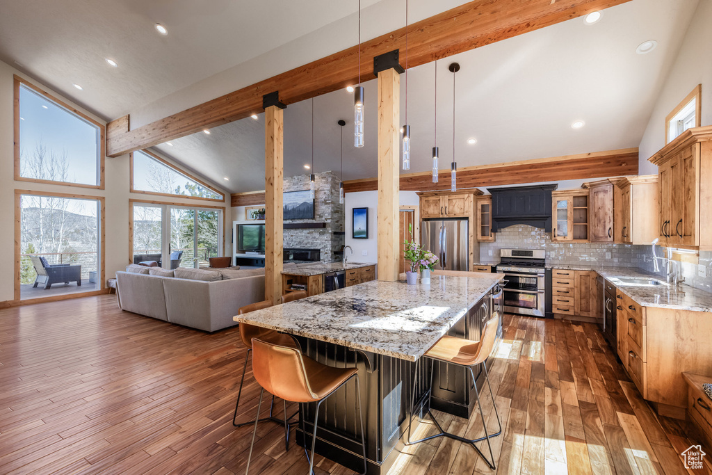 Kitchen with beam ceiling, a large island, high vaulted ceiling, a sink, and appliances with stainless steel finishes