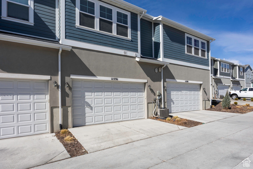 View of front facade with stucco siding, central air condition unit, a residential view, driveway, and a garage