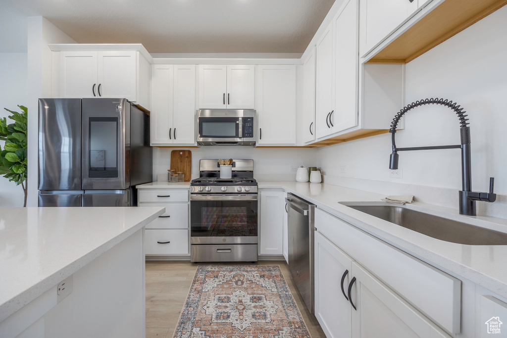 Kitchen featuring white cabinets, light wood-style flooring, light countertops, appliances with stainless steel finishes, and a sink