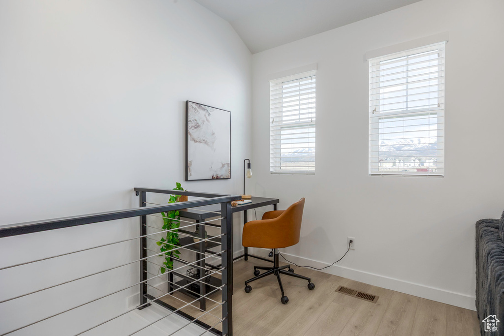 Office space featuring vaulted ceiling, baseboards, light wood finished floors, and visible vents