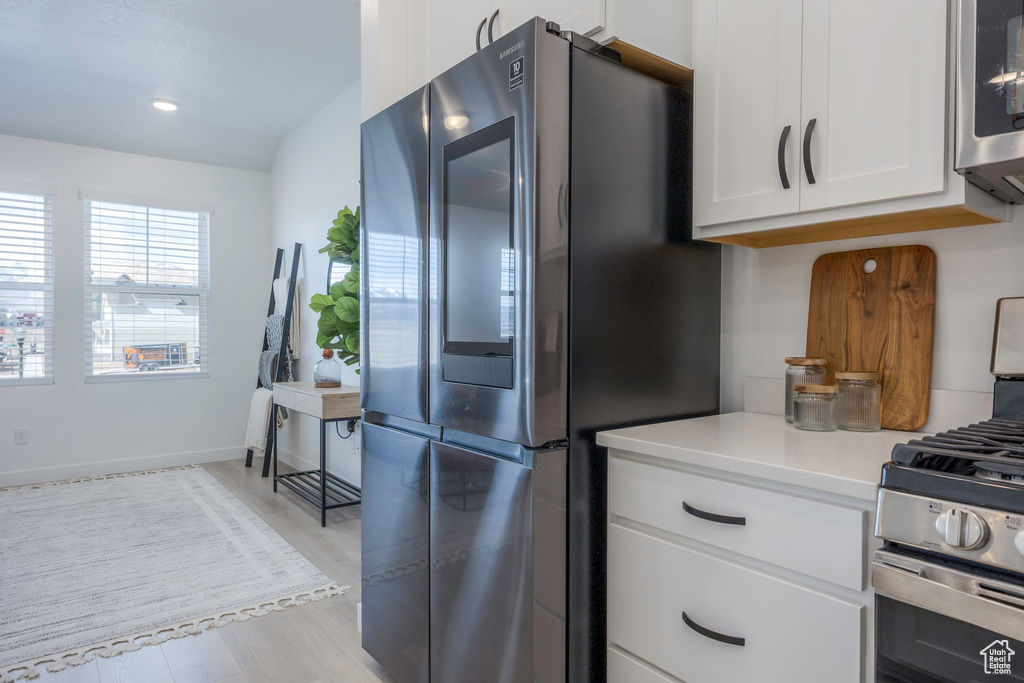 Kitchen featuring light countertops, appliances with stainless steel finishes, light wood-type flooring, baseboards, and white cabinets