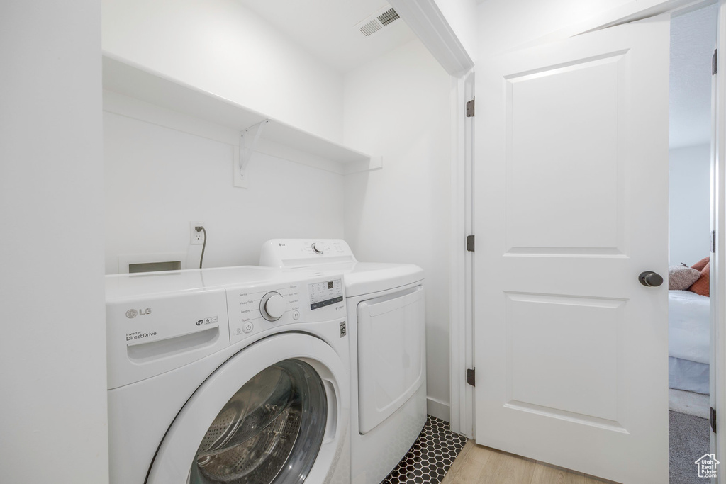 Clothes washing area with light wood-type flooring, washing machine and clothes dryer, laundry area, and visible vents
