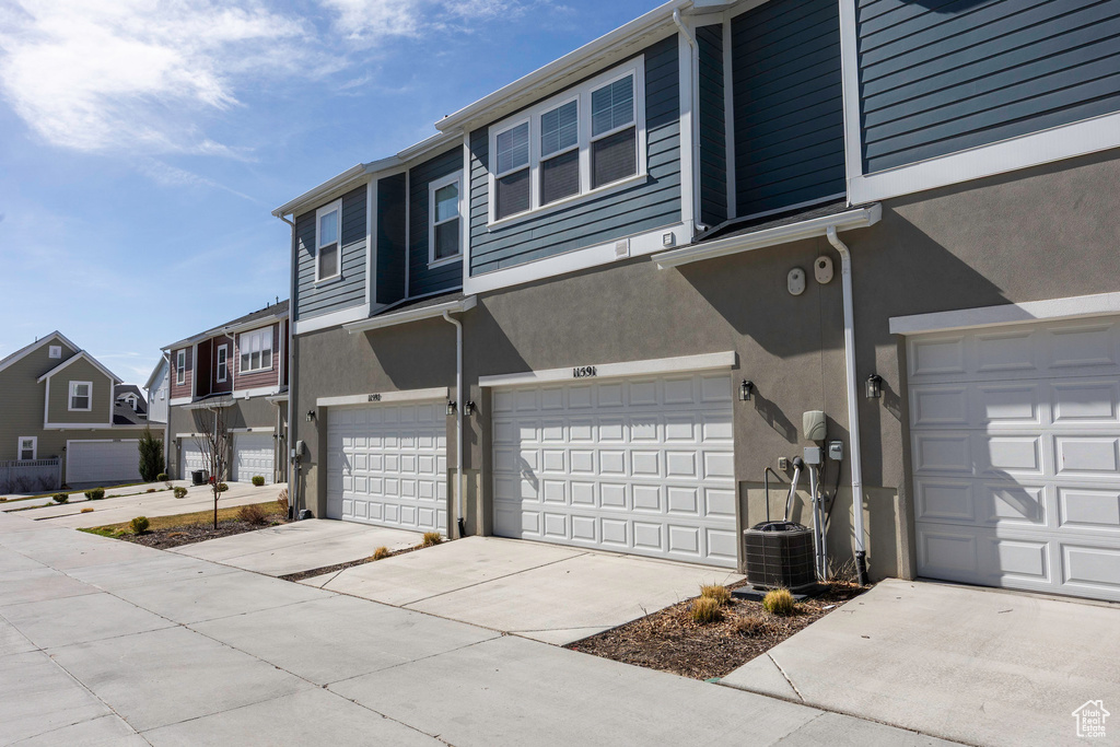 View of property exterior featuring driveway, central AC unit, a garage, a residential view, and stucco siding