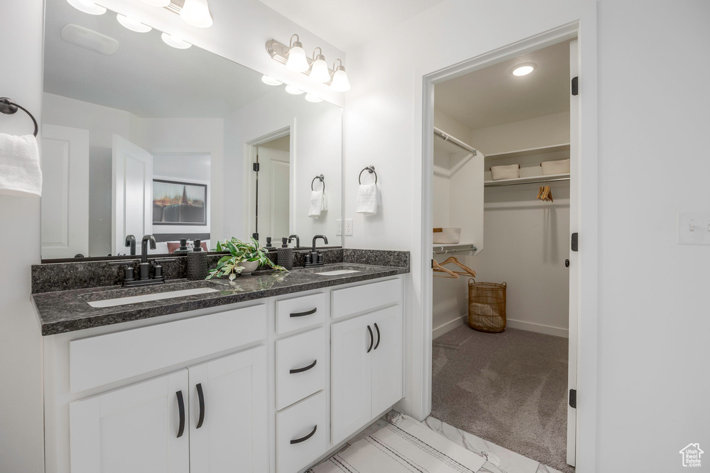 Bathroom featuring double vanity, a walk in closet, baseboards, and a sink
