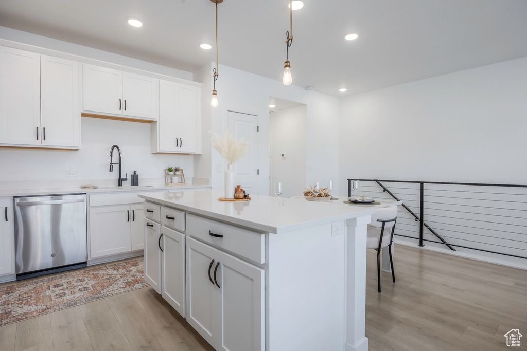 Kitchen featuring a sink, a kitchen island, dishwasher, white cabinets, and light wood-style floors