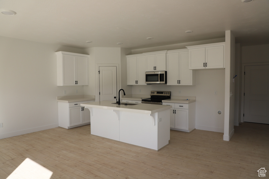 Kitchen with stainless steel appliances, a center island with sink, a sink, light wood-style floors, and white cabinets