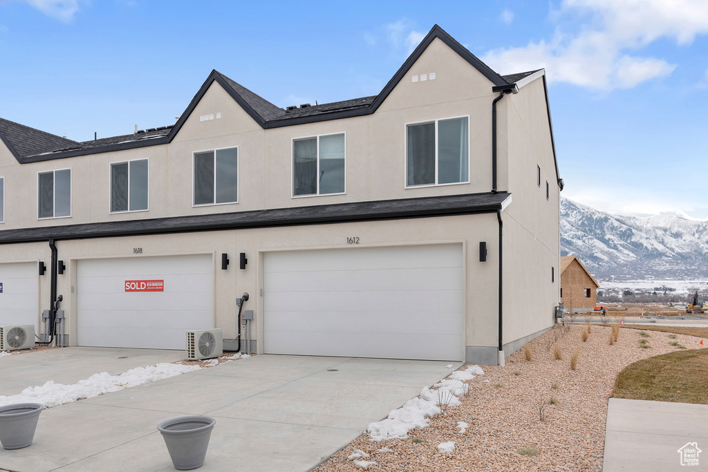 View of property with an attached garage, stucco siding, ac unit, driveway, and a mountain view