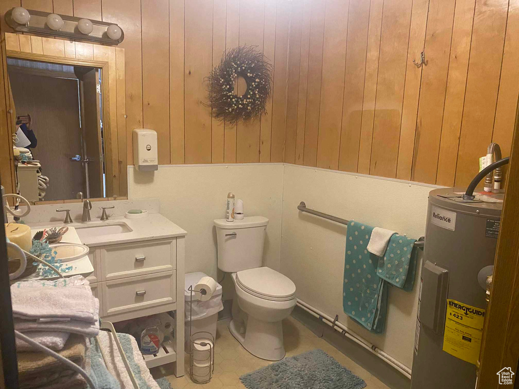 Bathroom with water heater, toilet, wooden walls, and vanity