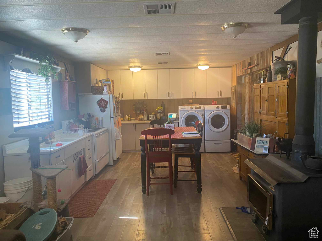 Kitchen featuring washing machine and clothes dryer, visible vents, white cabinetry, light wood-style floors, and a wood stove