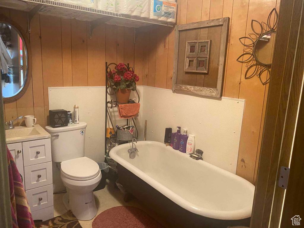 Full bathroom with a freestanding bath, toilet, wood walls, and vanity