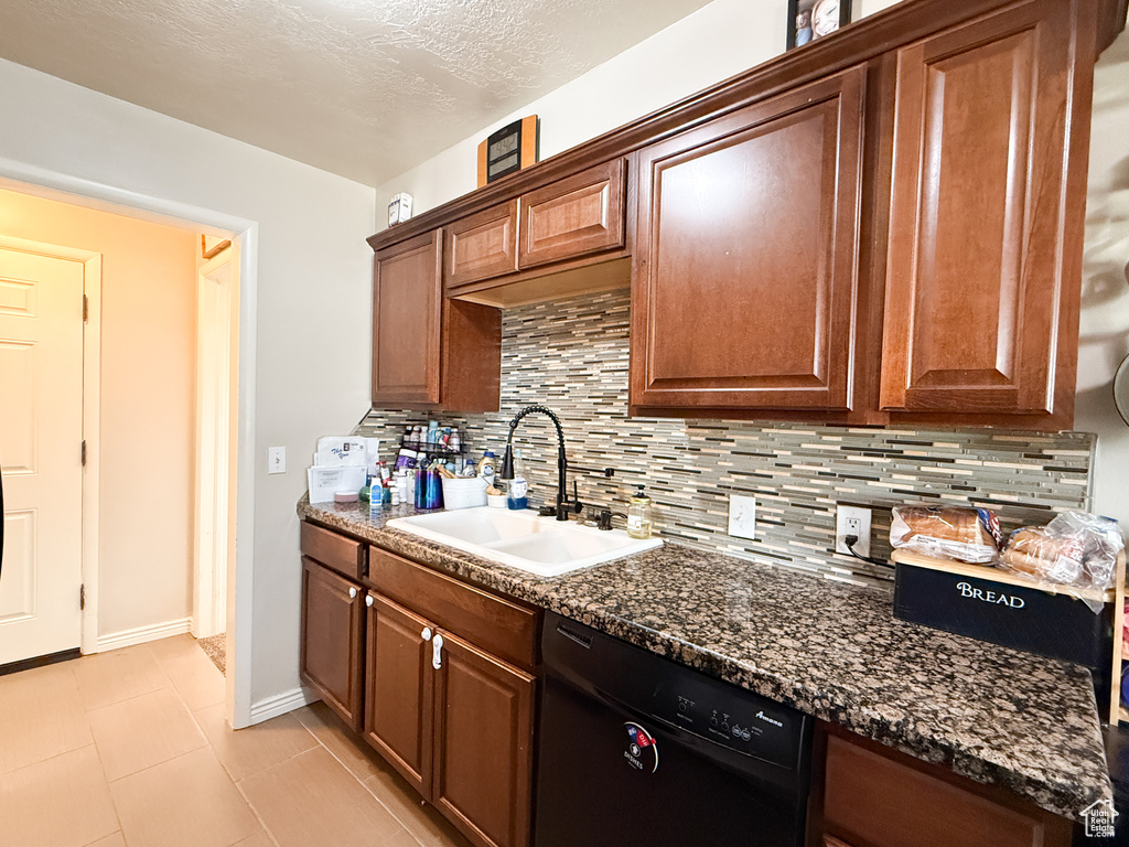 Kitchen with dark stone countertops, baseboards, backsplash, a sink, and dishwasher