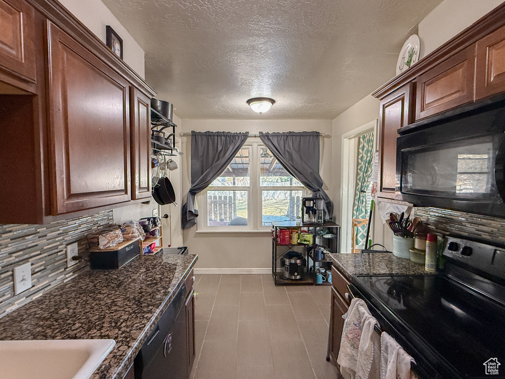 Kitchen featuring tasteful backsplash, a textured ceiling, dark stone countertops, baseboards, and black appliances