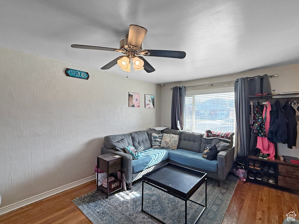 Living area with baseboards, ceiling fan, wood finished floors, and a textured wall