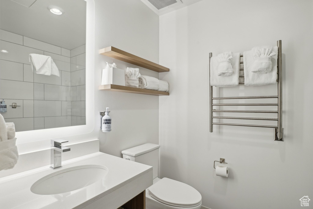 Full bathroom with tiled shower, toilet, vanity, radiator heating unit, and visible vents