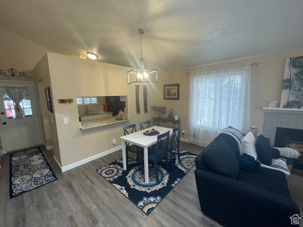 Dining area featuring vaulted ceiling, baseboards, a tiled fireplace, a notable chandelier, and wood finished floors