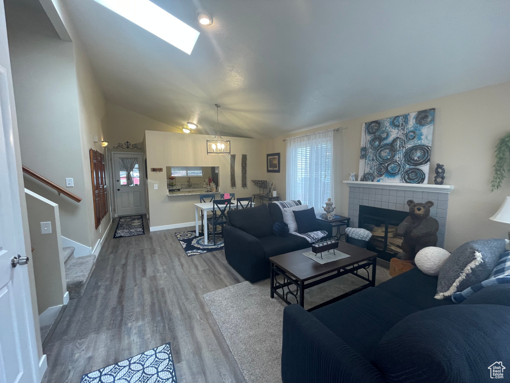 Living room featuring vaulted ceiling with skylight, stairway, a fireplace, wood finished floors, and baseboards