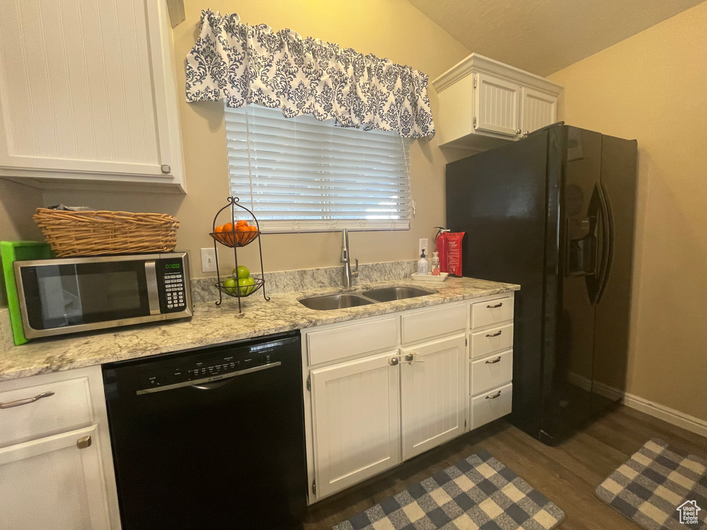 Kitchen with a sink, white cabinetry, light stone countertops, dark wood finished floors, and black appliances