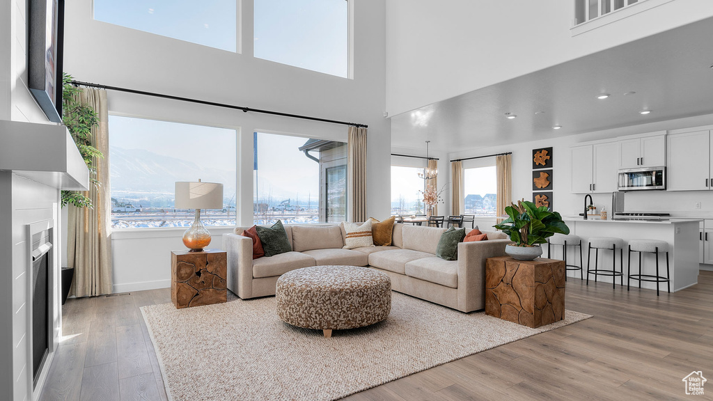 Living area featuring light wood-style floors, recessed lighting, a towering ceiling, and an inviting chandelier