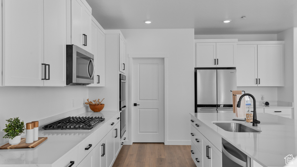 Kitchen featuring a sink, stainless steel appliances, wood finished floors, and white cabinetry