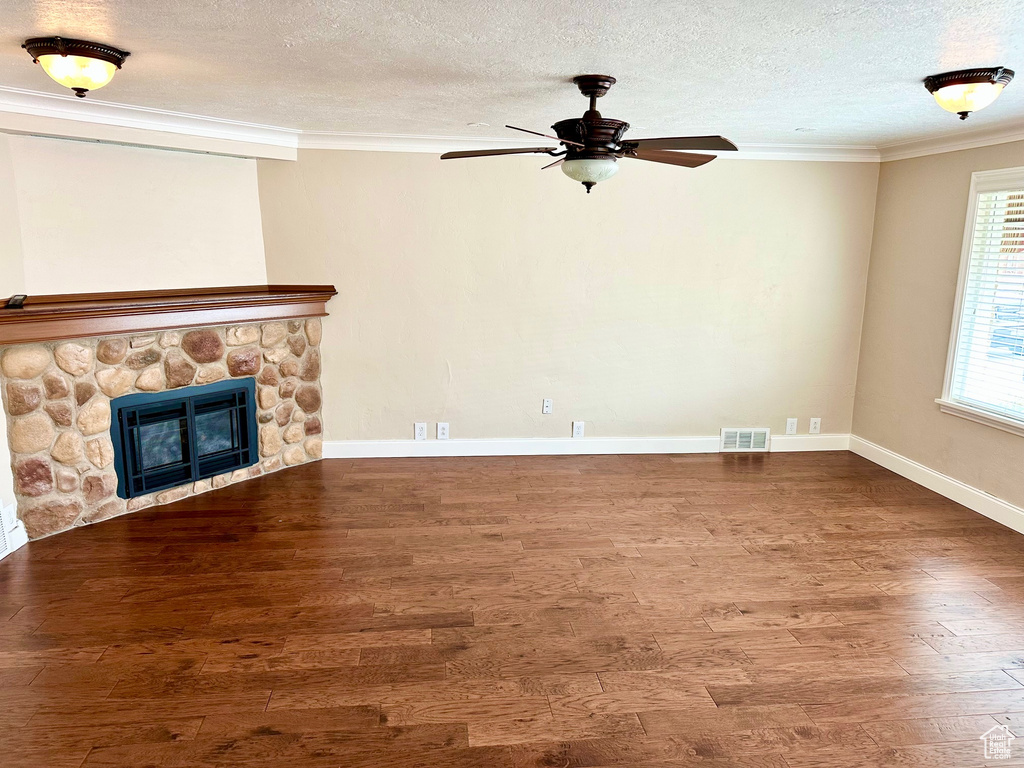 Unfurnished living room featuring crown molding, ceiling fan, visible vents, a stone fireplace, and wood finished floors