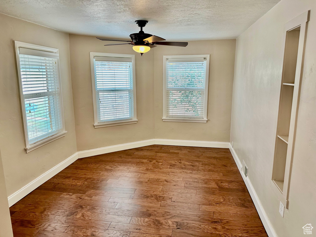 Unfurnished room featuring a textured ceiling, wood finished floors, baseboards, and a ceiling fan