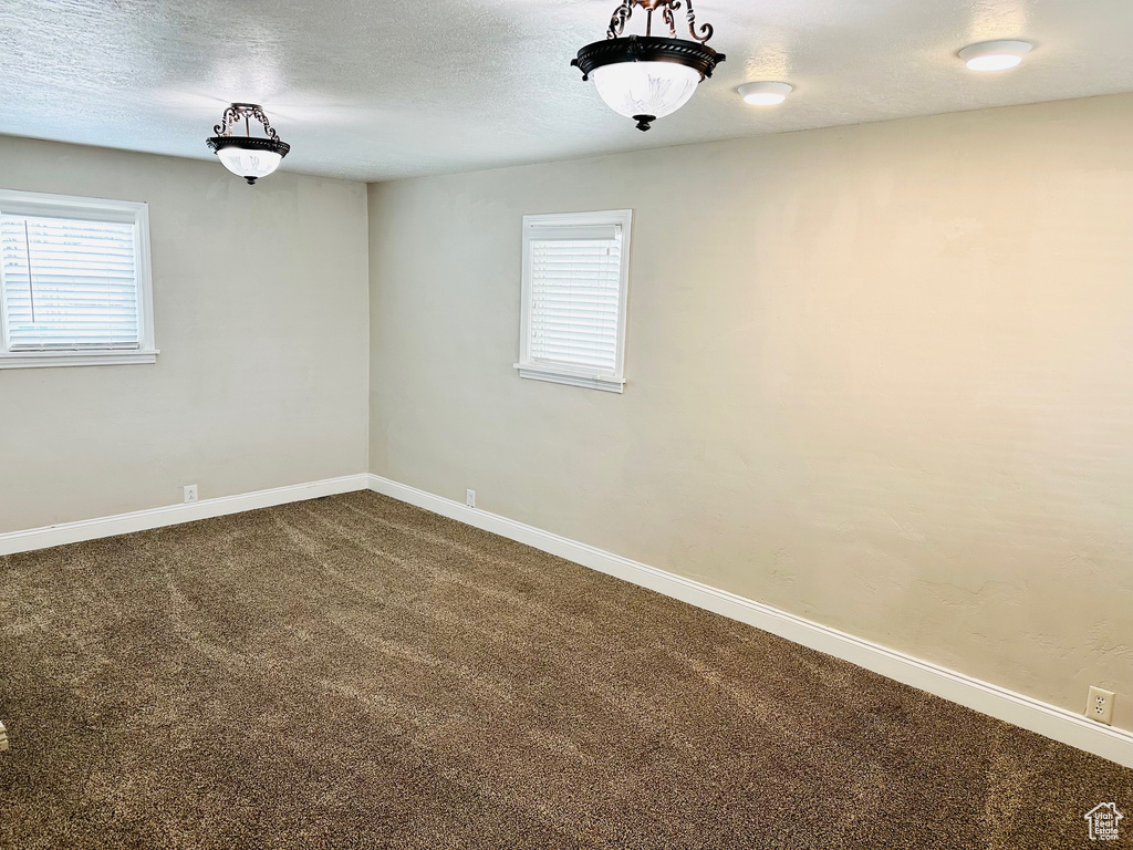 Spare room with a healthy amount of sunlight, dark colored carpet, and a textured ceiling