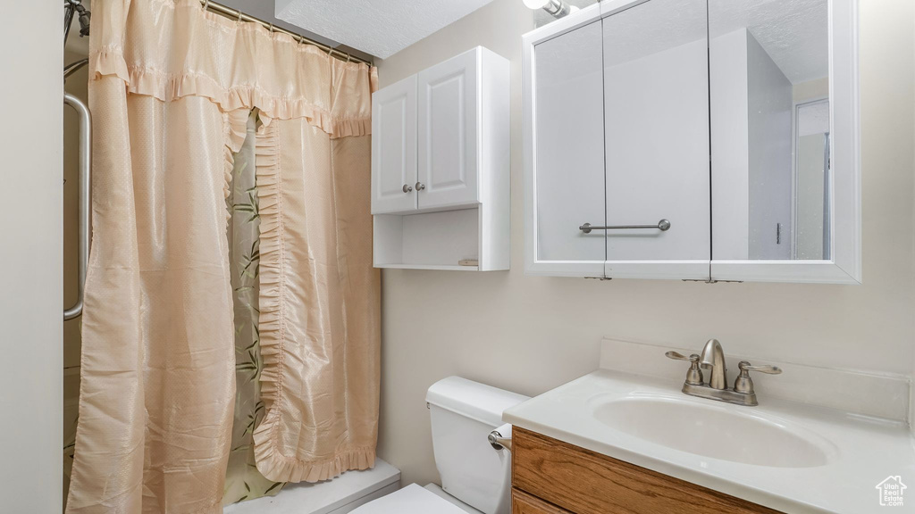 Bathroom featuring a shower with shower curtain, toilet, and vanity