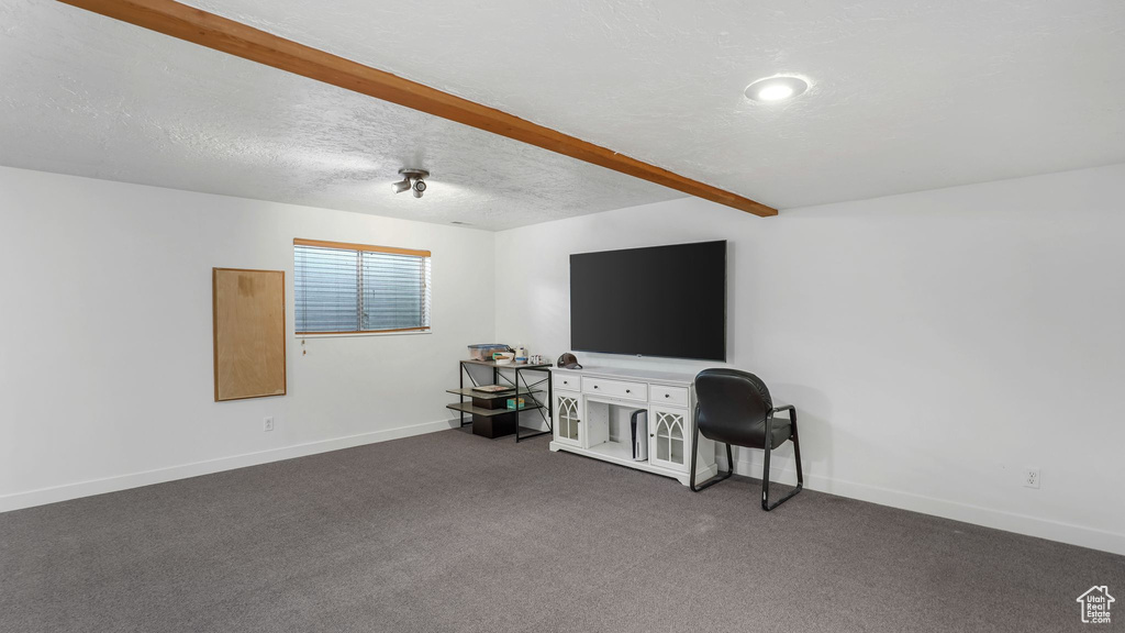 Interior space with baseboards, dark colored carpet, beamed ceiling, and a textured ceiling