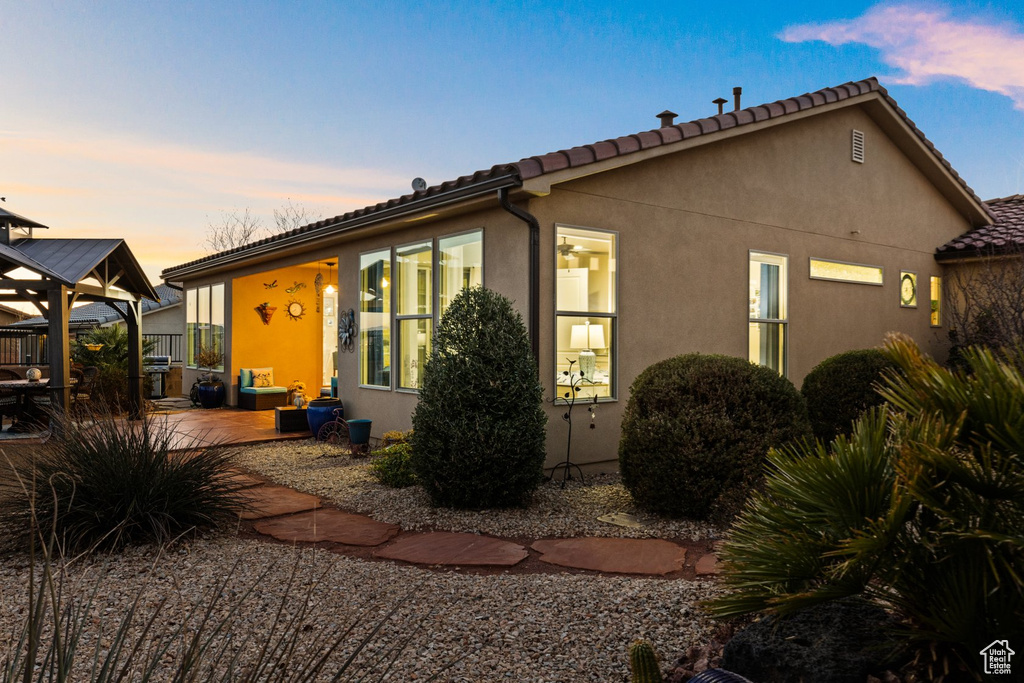 Back of property at dusk with a patio, a gazebo, stucco siding, and a tiled roof