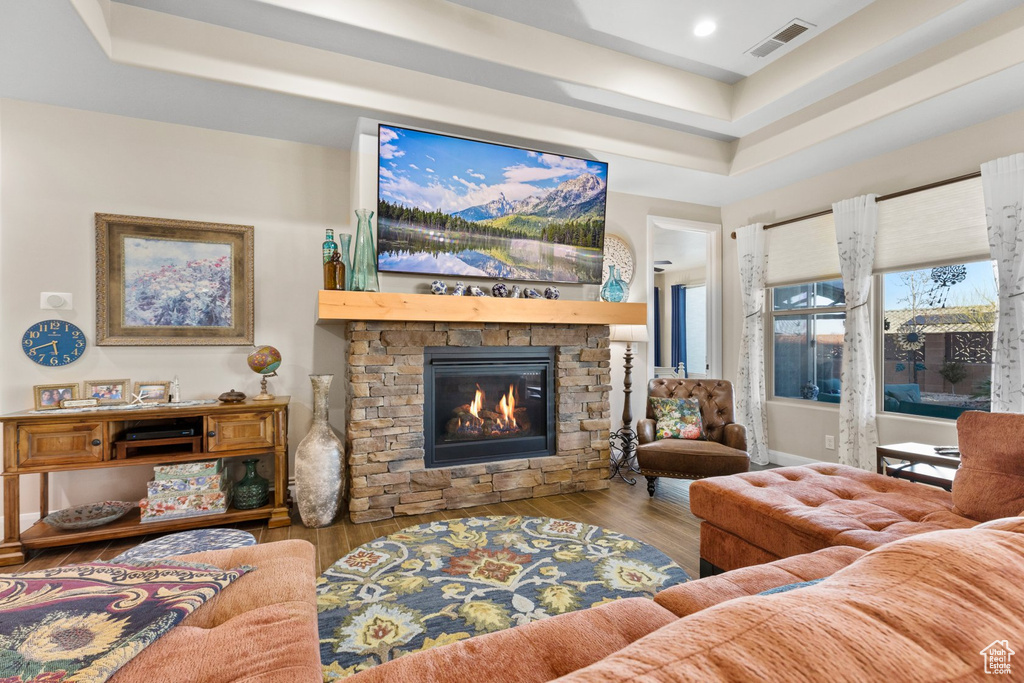 Living room with a raised ceiling, visible vents, recessed lighting, a fireplace, and wood finished floors